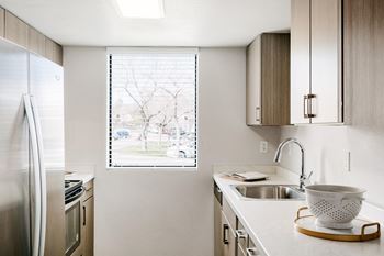 A kitchen with a stainless steel refrigerator and a window with blinds.